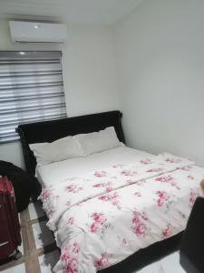 a bed with a white blanket with pink flowers on it at Terra Santa Lodgings in Accra