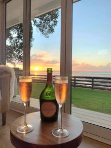 Una botella de champán y dos copas en una mesa. en Red Rock Cottage, beachfront luxury, en Clarks Beach