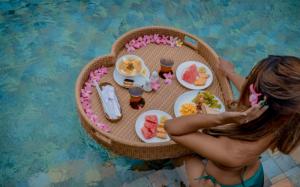 a woman sitting at a table with food in a pool at Umadhatu Resort by Amerta in Tabanan