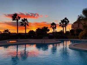 a swimming pool with palm trees and a sunset at Spirit of Mar Menor in Torre-Pacheco