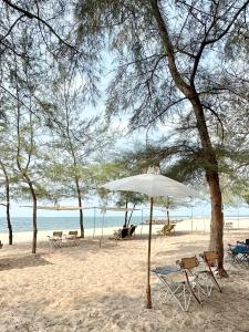 a beach with chairs and an umbrella on the sand at บ้านชายทะเล ที่พักติดทะเล ระยอง หาดแสงจันทร์ in Rayong