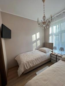 a white bedroom with two beds and a chandelier at Apartament Olivia Business Suite in Gdańsk