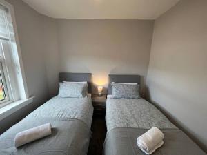two beds in a room with a lamp on a table at Cosy Cottage Apartment in Helensburgh