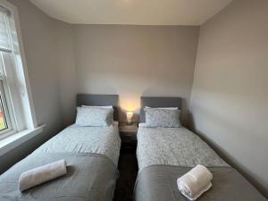 two beds in a room with a lamp on a table at Cosy Cottage Apartment in Helensburgh