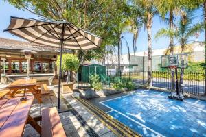 a swimming pool with an umbrella and a picnic table at Nightcap at High Flyer Hotel in Bankstown