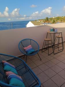 Un balcón con sillas, una mesa y el océano en Cibuqueira numéro 7, Centre ville, vue sur mer , plage à pied, en Le Moule