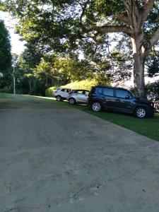 dois carros estacionados num parque de estacionamento ao lado de uma árvore em Hospedagem Casa Branca Localizada em um bairro nobre de Capitólio, Escarpas do Lago em Capitólio