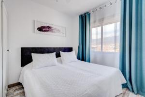 a bedroom with a white bed with blue curtains and a window at BuenaVista Palmeras in Costa Adeje in Adeje +51 photos