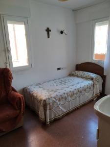 um quarto com uma cama, uma cadeira e 2 janelas em Albergue La Esperanza de la Sagrada Familia em Melgar de Fernamental