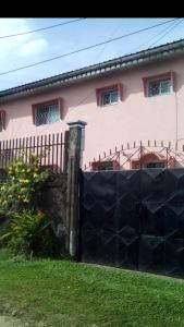 uma cerca em frente a uma casa cor-de-rosa em Vicky Appartements Palmengarten Douala Maképè Belavie em Douala