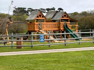 un parque infantil con una casa de madera con un tobogán en Bude holiday home, en Bude