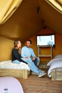 a man and woman sitting on beds in a tent at Sahara Stay in Vluchtenburg