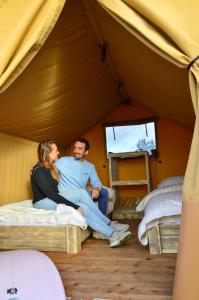 a man and woman sitting on beds in a tent at Sahara Stay in Vluchtenburg