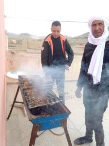 dos hombres están cocinando comida en una parrilla en Maison D'hôtes Chez Bassou Agoudal, en Agoudal