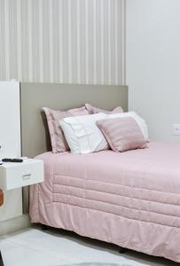 uma cama com lençóis cor-de-rosa e brancos e uma mesa branca em Lukinhas Pousada em Nobres