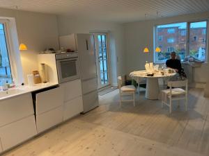 eine Küche mit einem Tisch und einer Person, die an einem Tisch sitzt in der Unterkunft Stor lys lejlighed med terrasse og altan in Helsingør + 8 Fotos