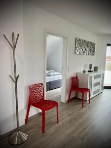 a living room with two red chairs and a bedroom at LUX Ferienwohnungen in Hepbach