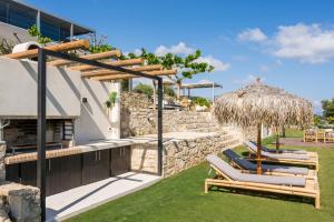 eine Terrasse mit Liegestühlen und einem Strohschirm in der Unterkunft OliveNest Chania Executive Villa in Perivólia