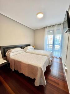 2 łóżka w pokoju z drewnianymi podłogami i oknami w obiekcie Apartamento Somocuevas w mieście Liencres