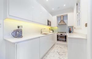 Biała kuchnia z białymi szafkami i urządzeniami w obiekcie GARDEN Flat in Posh MEWS w Londynie