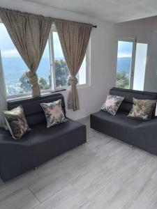 a living room with two black couches and windows at El Mirador de LucyMelia in Guarne