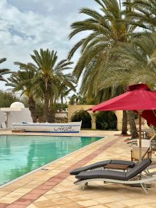 uma piscina com duas espreguiçadeiras e um guarda-sol vermelho em Le Patio de Mezraya em Mezraya
