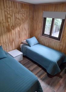 two beds in a room with wood paneled walls at Borde Rio Coyhaique Cabaña y Tinaja in Coihaique