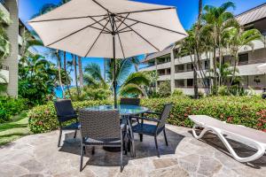 - une table et des chaises avec un parasol sur la terrasse dans l'établissement Paradise Found at White Sands Village 105, à Kailua-Kona