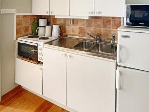 eine Küche mit weißen Schränken, einer Spüle und einem Kühlschrank in der Unterkunft Holiday home Ronneby VI in Ronneby