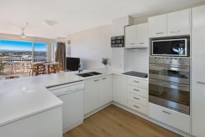 a kitchen with white cabinets and a large window at Beachside Resort Kawana Waters in Buddina