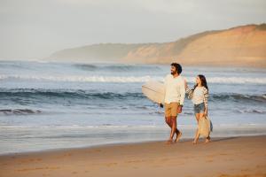 a man and woman walking on the beach with a surfboard at RACV Torquay Resort in Torquay