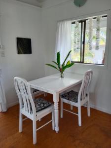 Una mesa blanca y dos sillas con una planta. en Poppies Beach Bach en Matavera