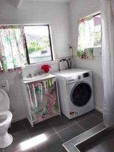 a bathroom with a washing machine and a window at Poppies Beach Bach in Matavera