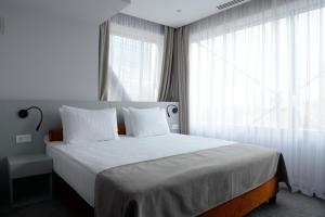 1 dormitorio con 1 cama con sábanas blancas y ventanas en Premier Hotel Miskolc, en Miskolc