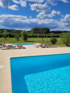 a blue swimming pool with chairs and a field at Hôtel La Bastide d'Iris in Vagnas