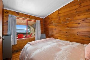 1 dormitorio con paredes de madera, 1 cama y ventana en Lakeside Lookout - Lake Tarawera Holiday Home, en Lake Tarawera