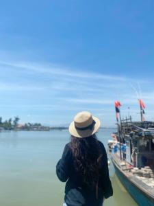Una donna con un cappello in piedi accanto a una barca. di Sunshine villa thuan an a Hue