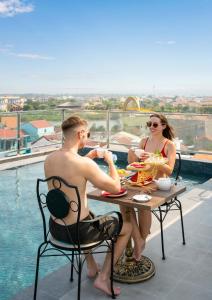 um homem e uma mulher sentados numa mesa perto de uma piscina em Hoi An Babylon Riverside Hotel & Spa em Hoi An