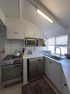 a white kitchen with a stove and a sink at Die Boomhuis. Pearly Beach in Pearly Beach