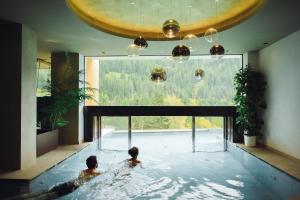 zwei Personen in einem Pool mit großem Fenster in der Unterkunft Latemar - Hotel Suites Spa in Soraga