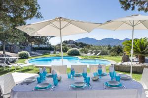 einen Tisch mit Stühlen und einen Sonnenschirm neben einem Pool in der Unterkunft Villa Cava Del Tom Luxury in Porto Rotondo
