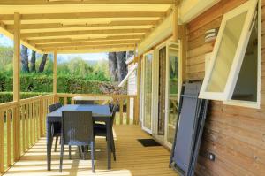 a deck with a table and chairs and a television at Flower Camping Les Mijeannes in Rieux-de-Pelleport