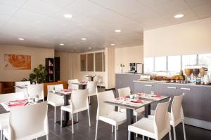 uma sala de jantar com mesas e cadeiras brancas e uma cozinha em Séjours & Affaires Paris Vincennes em Vincennes