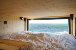 Bett in einem Zimmer mit einem großen Fenster in der Unterkunft Tiny House Nature 3 Zur Kuhweide - Green Tiny Village Harlesiel in Carolinensiel