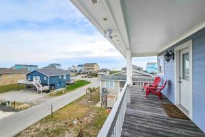a porch of a blue house with a red chair at HB261 Rosie's Rendezvous in Holden Beach