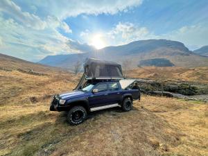 a blue truck parked on a field with mountains in the background at Amelia Rooftop Tent Rental from ElectricExplorers in Hawkshead