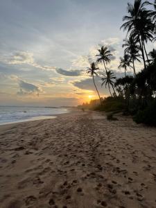 una playa con palmeras y el océano al atardecer en All View Resort en Tangalle