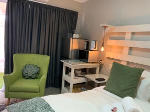 een slaapkamer met een bed, een stoel en een televisie bij Meraki Upmarket Guesthouse in Rustenburg