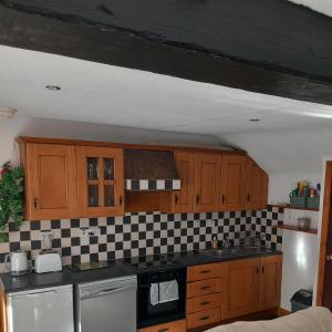 a kitchen with wooden cabinets and a checkered wall at Eddie's Roadside Thatched Cottage 