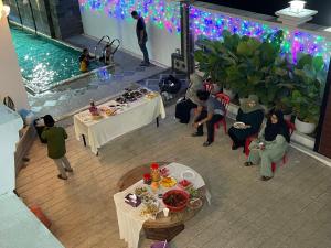 grupa osób siedzących przy stolikach w pokoju z basenem w obiekcie Aainaa Villa Homestay w mieście Pasir Mas